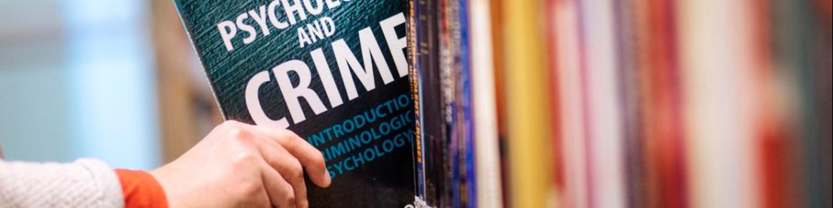 Käsi ot­taa kir­ja­hyl­lys­tä kir­jan Psyc­ho­lo­gy and Cri­me.