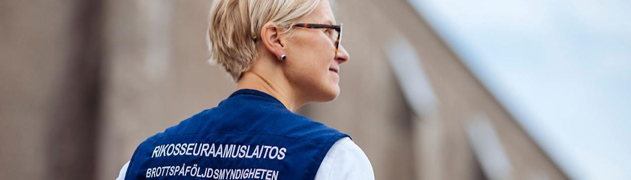 Nainen seisoo muuria vasten. Hänellä on yllään liivi